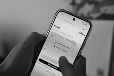 A photograph of a person holding a phone with the Guardian app open, showing the sign-in screen. Photograph: Mahesh Makani